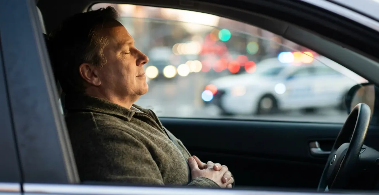 Vue latérale d'un conducteur pratiquant un exercice de respiration profonde lors d'un arrêt, mains relâchées sur les genoux